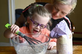 Lucy sitting on her mum Julie’s knee at a table mixing flour in a big glass bowl. Picture: Michael Cooper