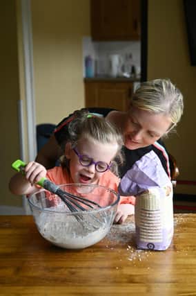 Lucy sitting on her mum Julie’s knee at a table mixing flour in a big glass bowl. Picture: Michael Cooper