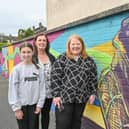 Justice Minister Naomi Long is pictured with Theresa Maginn and Aoife Maginn. Aoife was one of a group of young people who helped create the mural in the background of the picture. Members of the youth group worked with artist Conor McGinley to create a mural situated in Slieveshan Park for the whole community to enjoy.