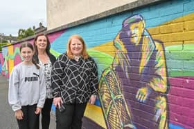 Justice Minister Naomi Long is pictured with Theresa Maginn and Aoife Maginn. Aoife was one of a group of young people who helped create the mural in the background of the picture. Members of the youth group worked with artist Conor McGinley to create a mural situated in Slieveshan Park for the whole community to enjoy.